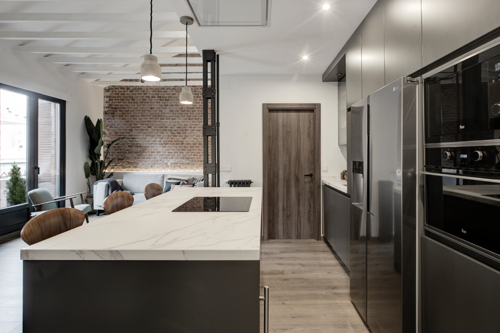 This is an example of a mid-sized industrial open plan kitchen in Madrid with a single-bowl sink, glass-front cabinets, grey cabinets, marble benchtops, panelled appliances, laminate floors, with island and brown floor.