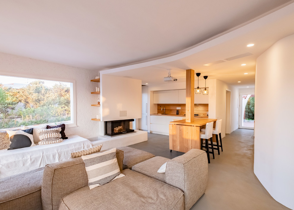 Photo of a mid-sized beach style open concept living room in Other with white walls, concrete floors, a corner fireplace, a plaster fireplace surround and grey floor.