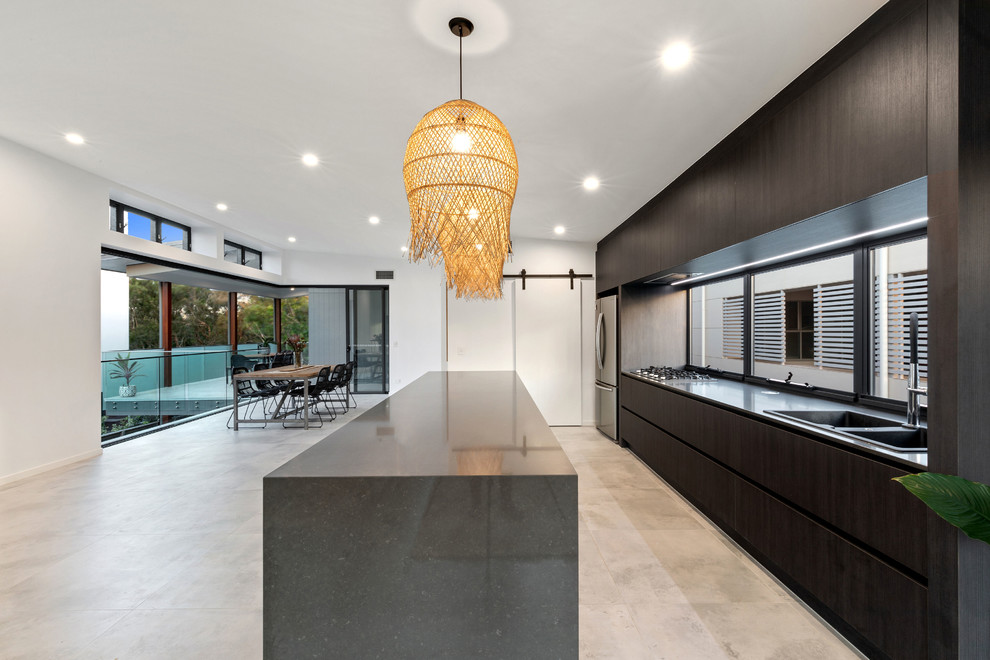 Beach style kitchen in Sunshine Coast with a drop-in sink, flat-panel cabinets, black cabinets, granite benchtops, glass sheet splashback, black appliances, porcelain floors, with island, grey floor and black benchtop.