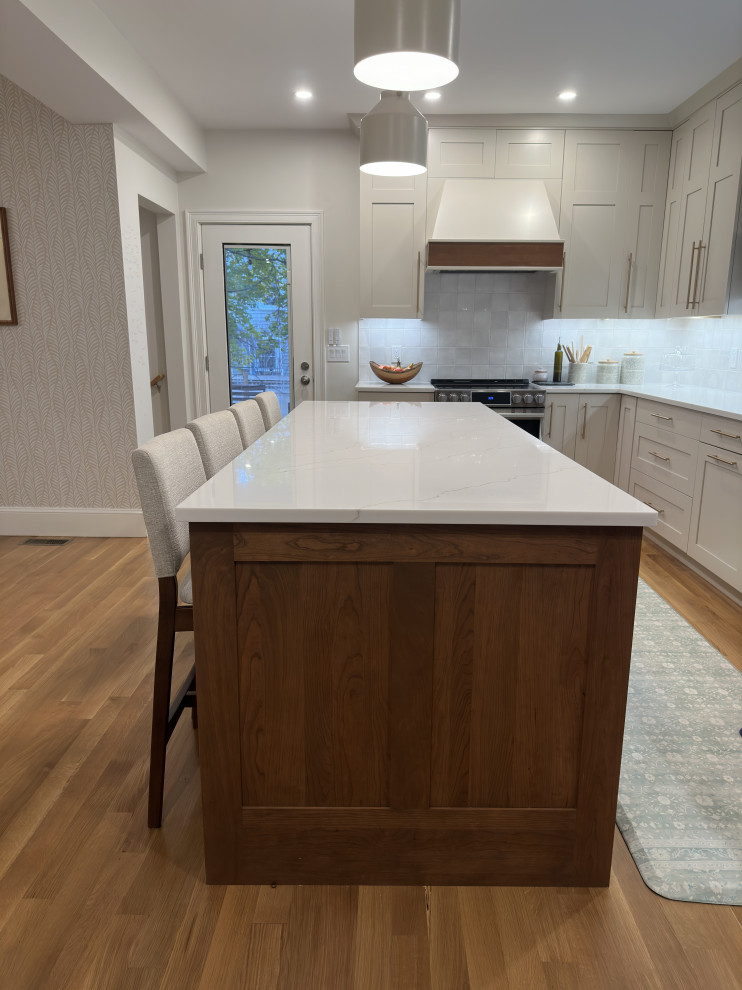 This is an example of a mid-sized midcentury l-shaped eat-in kitchen in Boston with an undermount sink, flat-panel cabinets, medium wood cabinets, quartz benchtops, white splashback, ceramic splashback, stainless steel appliances, light hardwood floors, with island, brown floor and white benchtop.
