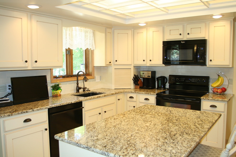 Photo of a large traditional u-shaped eat-in kitchen in Grand Rapids with recessed-panel cabinets, beige cabinets, quartz benchtops, with island, an undermount sink, white splashback, subway tile splashback, black appliances, beige benchtop, porcelain floors and beige floor.