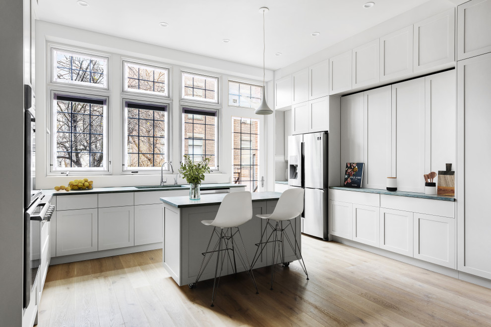 Photo of an expansive transitional u-shaped eat-in kitchen in New York with a drop-in sink, flat-panel cabinets, white cabinets, granite benchtops, white splashback, ceramic splashback, stainless steel appliances, light hardwood floors, with island, beige floor and green benchtop.