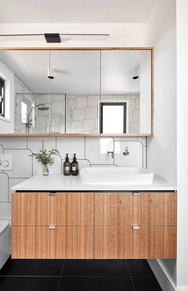 Contemporary bathroom in Melbourne with flat-panel cabinets, medium wood cabinets, white tile, white walls, a vessel sink, black floor, white benchtops, a single vanity and a floating vanity.