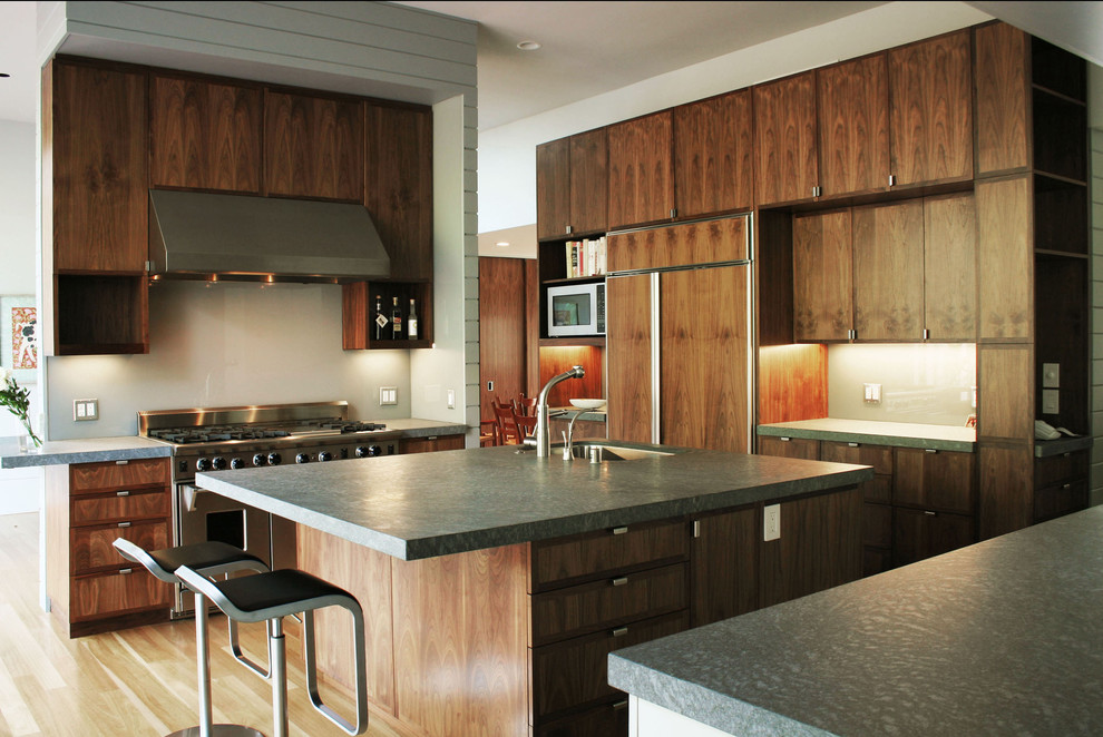 Photo of a transitional u-shaped eat-in kitchen in San Francisco with flat-panel cabinets, dark wood cabinets, white splashback, with island, an undermount sink, stainless steel appliances, light hardwood floors, glass sheet splashback and brown floor.