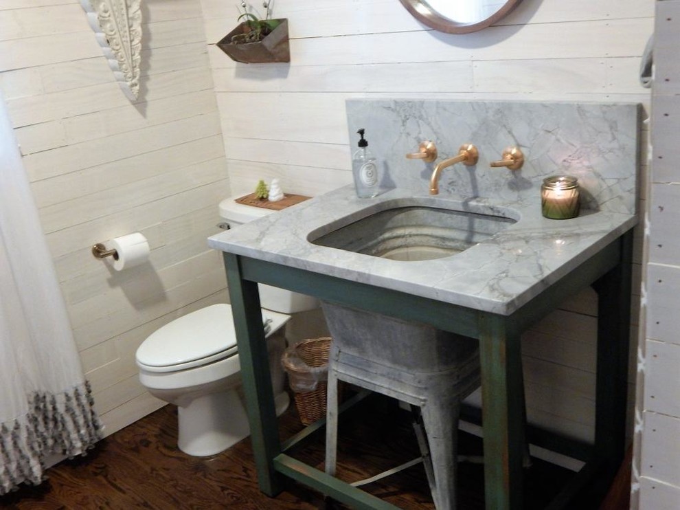 This is an example of a mid-sized country powder room in St Louis with furniture-like cabinets, distressed cabinets, a two-piece toilet, white walls, dark hardwood floors, marble benchtops, a console sink and brown floor.