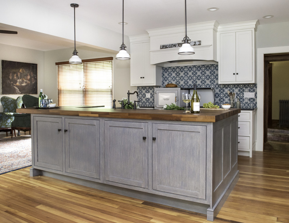 Photo of a mid-sized country galley open plan kitchen in Boston with a farmhouse sink, beaded inset cabinets, white cabinets, wood benchtops, blue splashback, cement tile splashback, panelled appliances, medium hardwood floors, with island, brown floor and black benchtop.