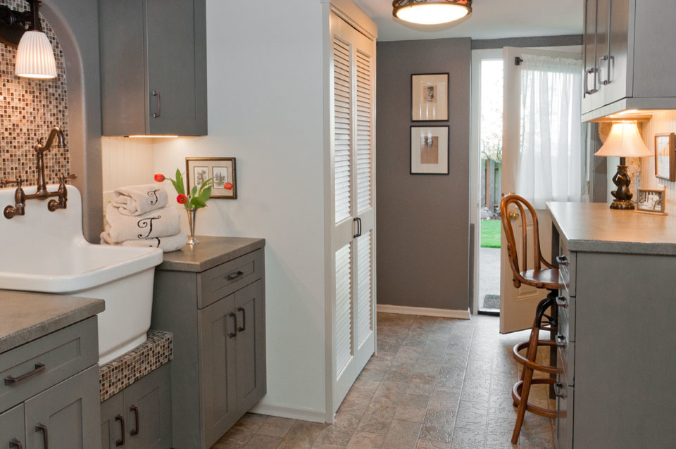 Photo of a small arts and crafts galley utility room in Seattle with a farmhouse sink, shaker cabinets, grey cabinets, laminate benchtops, grey walls, vinyl floors and a stacked washer and dryer.