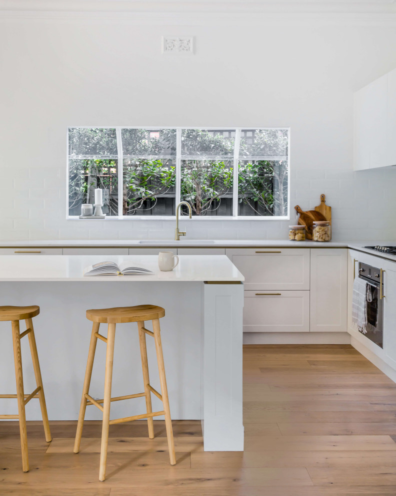 Design ideas for a mid-sized traditional l-shaped open plan kitchen in Melbourne with shaker cabinets, white cabinets, limestone benchtops, white splashback, ceramic splashback, stainless steel appliances, with island, white benchtop, a double-bowl sink, painted wood floors and brown floor.