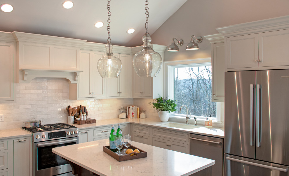 Example of a transitional medium tone wood floor, brown floor and vaulted ceiling eat-in kitchen design with an undermount sink, shaker cabinets, white cabinets, quartz countertops, white backsplash, ceramic backsplash, stainless steel appliances, an island and white countertops