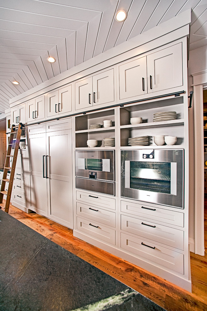 Large mountain style l-shaped medium tone wood floor and brown floor eat-in kitchen photo with an undermount sink, shaker cabinets, gray cabinets, soapstone countertops, black backsplash, stone slab backsplash, stainless steel appliances and two islands