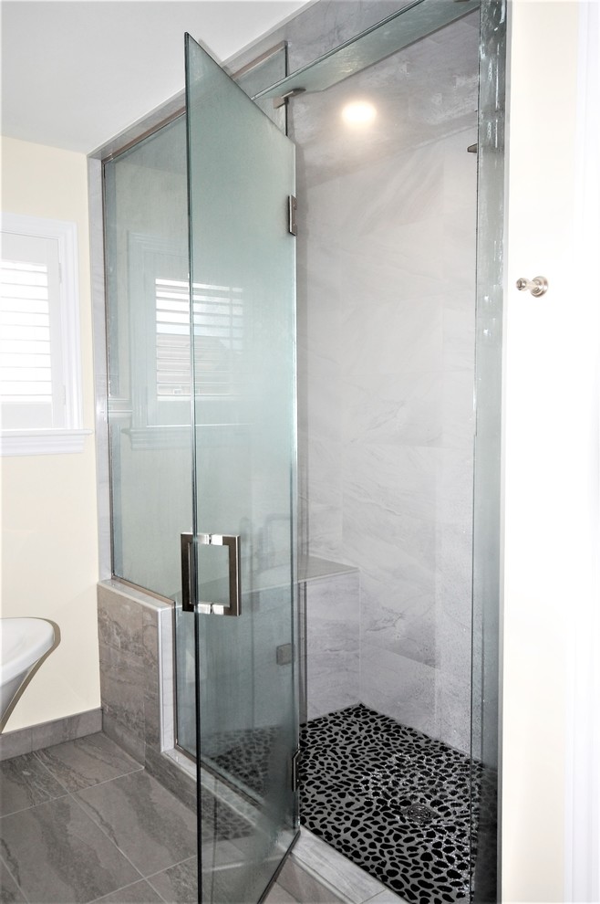 Photo of a large contemporary master wet room bathroom in Ottawa with shaker cabinets, grey cabinets, a freestanding tub, gray tile, porcelain tile, yellow walls, pebble tile floors, an undermount sink, engineered quartz benchtops, grey floor and a hinged shower door.