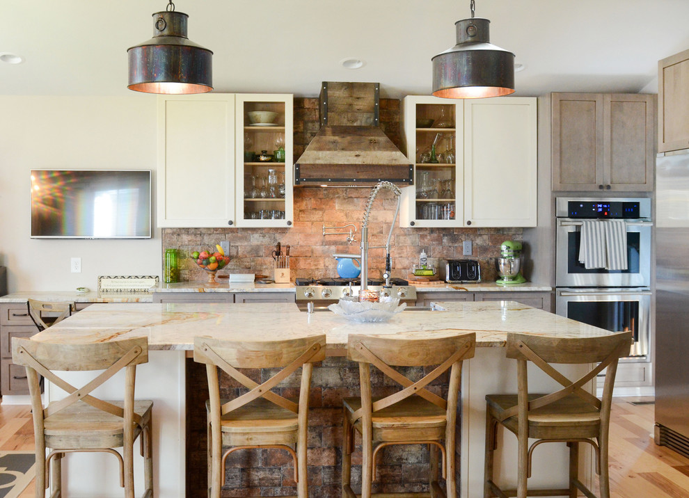 Inspiration for a large country u-shaped open plan kitchen in Columbus with a farmhouse sink, shaker cabinets, distressed cabinets, granite benchtops, multi-coloured splashback, brick splashback, stainless steel appliances, medium hardwood floors, with island and brown floor.