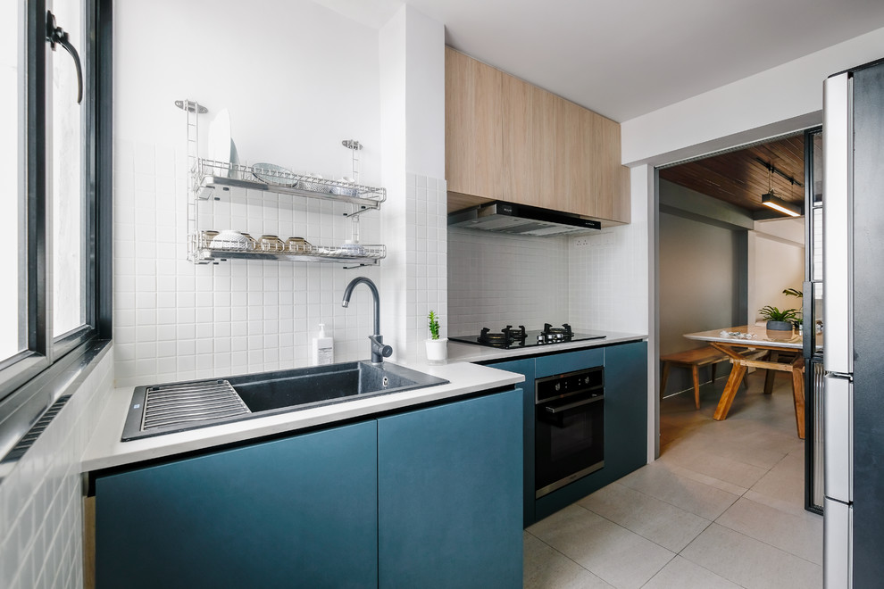 Contemporary galley separate kitchen in Singapore with a drop-in sink, flat-panel cabinets, blue cabinets, white splashback, stainless steel appliances, no island, grey floor and white benchtop.