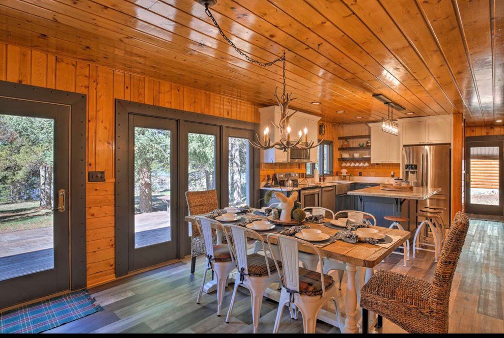 Inspiration for a mid-sized country l-shaped open plan kitchen in Boise with a farmhouse sink, recessed-panel cabinets, grey cabinets, stainless steel benchtops, stainless steel appliances, medium hardwood floors, with island, brown floor and grey benchtop.
