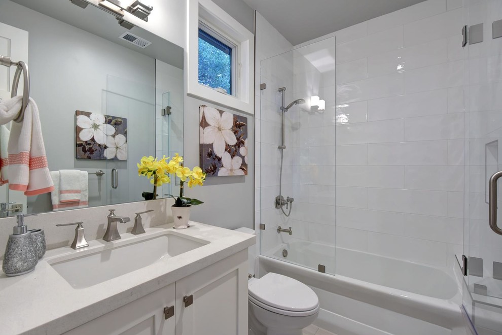 Inspiration for a large transitional 3/4 bathroom in San Francisco with shaker cabinets, white cabinets, an alcove tub, a shower/bathtub combo, white tile, grey walls, an undermount sink, a hinged shower door, a one-piece toilet, subway tile, porcelain floors, engineered quartz benchtops, grey floor and white benchtops.