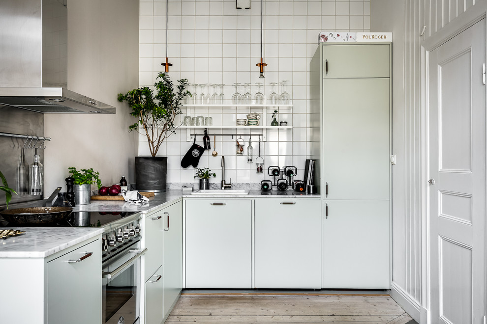 Photo of a scandinavian l-shaped kitchen in Stockholm with flat-panel cabinets, green cabinets, marble benchtops, light hardwood floors, no island, a drop-in sink, white splashback, stainless steel appliances and beige floor.