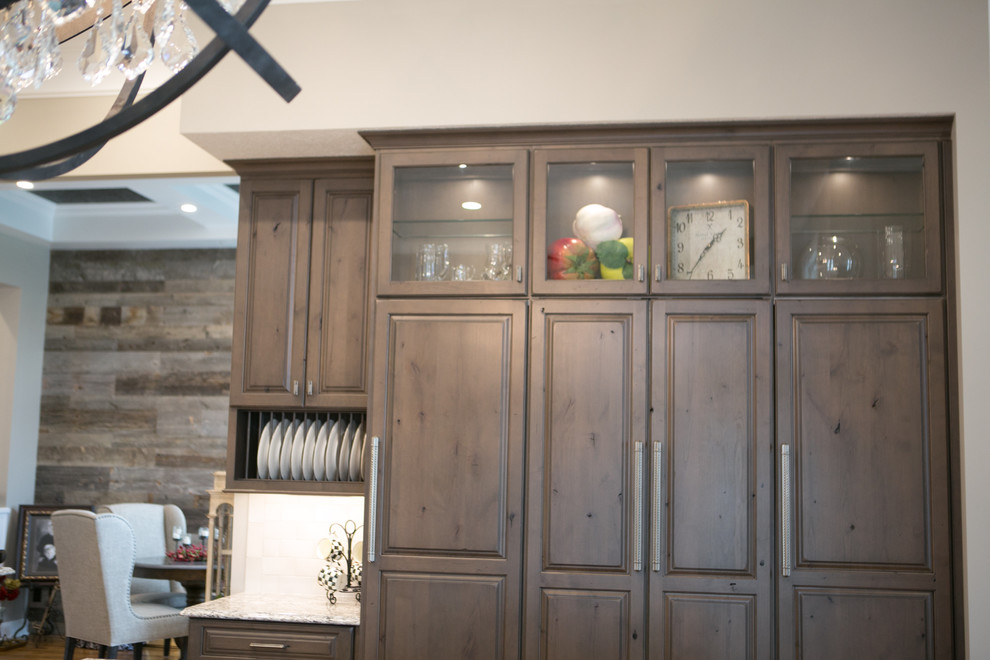 Inspiration for a large transitional u-shaped medium tone wood floor and brown floor kitchen remodel in Indianapolis with a farmhouse sink, raised-panel cabinets, dark wood cabinets, granite countertops, white backsplash, subway tile backsplash, paneled appliances, an island and multicolored countertops