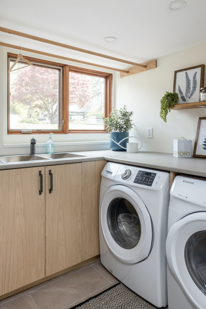 Photo of a mid-sized contemporary galley utility room in Vancouver with flat-panel cabinets, light wood cabinets, laminate benchtops, white walls, a side-by-side washer and dryer and grey benchtop.