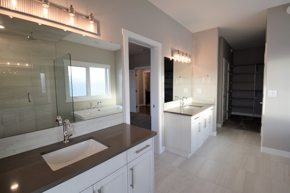 Photo of a large transitional master bathroom in Calgary with recessed-panel cabinets, white cabinets, a freestanding tub, a corner shower, gray tile, marble, grey walls, porcelain floors, an undermount sink, engineered quartz benchtops, grey floor and a hinged shower door.