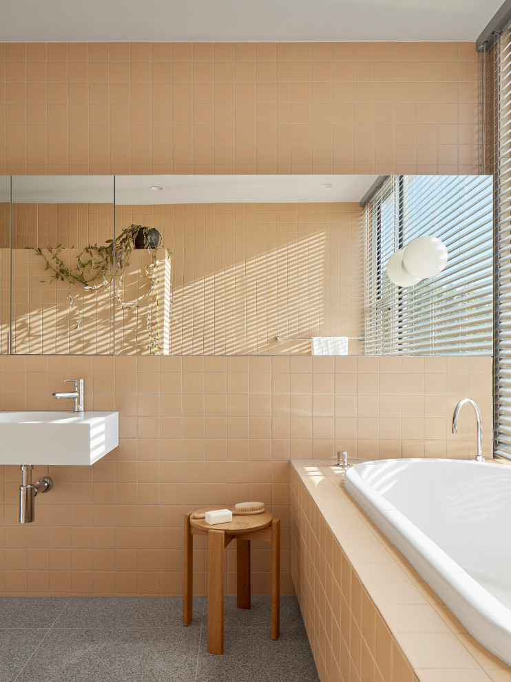 Modelo de cuarto de baño infantil, único y flotante moderno de tamaño medio con puertas de armario blancas, bañera encastrada, ducha empotrada, baldosas y/o azulejos naranja, suelo gris y encimeras blancas