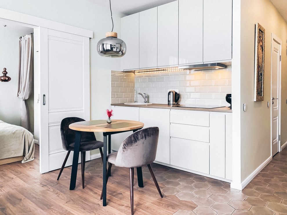 Photo of a small scandinavian single-wall open plan kitchen in Moscow with an undermount sink, flat-panel cabinets, white cabinets, white splashback, multiple islands and brown floor.