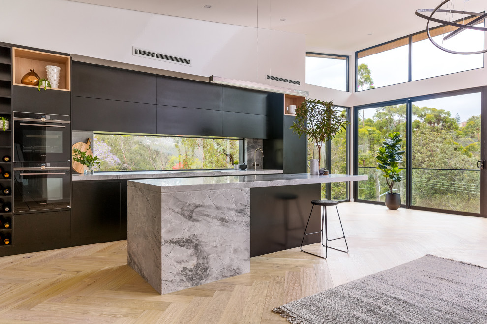 Photo of a large modern kitchen in Sydney with black cabinets, marble benchtops, marble splashback, black appliances and with island.