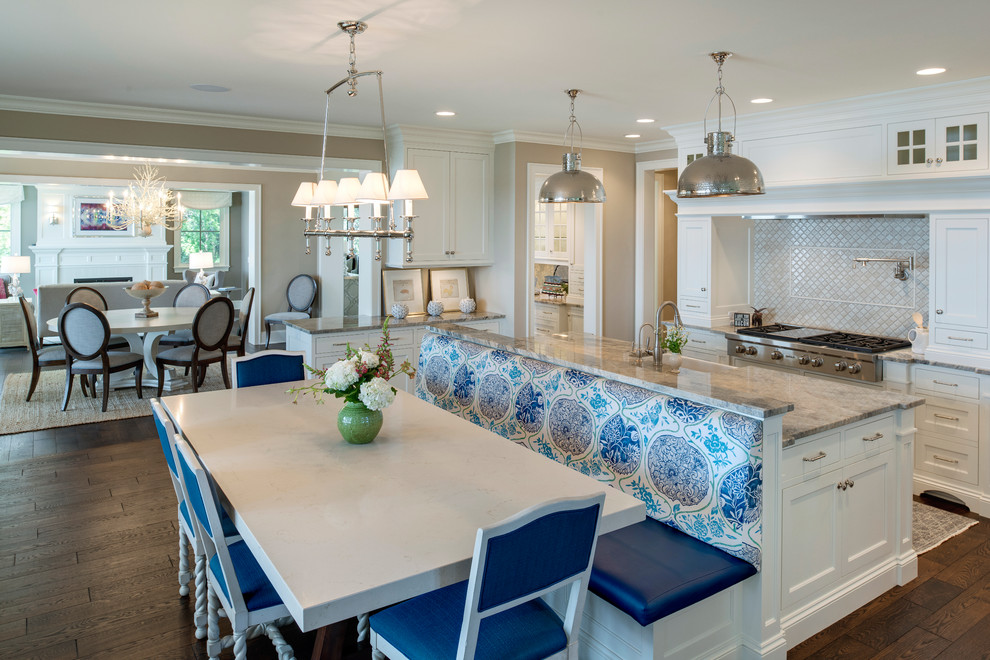 Photo of an expansive beach style u-shaped eat-in kitchen in Minneapolis with shaker cabinets, white cabinets, beige splashback, stainless steel appliances, dark hardwood floors, with island, a farmhouse sink, marble benchtops, mosaic tile splashback and brown floor.