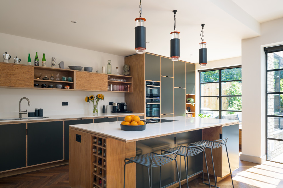 Scandinavian kitchen in London with a double-bowl sink, flat-panel cabinets, black cabinets, white splashback, black appliances, medium hardwood floors, with island and white benchtop.