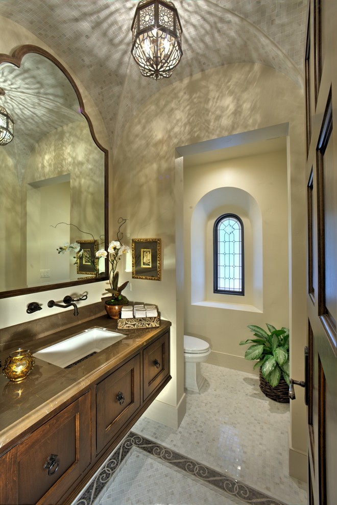 Inspiration for an expansive mediterranean powder room in Sacramento with recessed-panel cabinets, dark wood cabinets, a one-piece toilet, black and white tile, white walls, mosaic tile floors, an undermount sink, limestone benchtops and white floor.