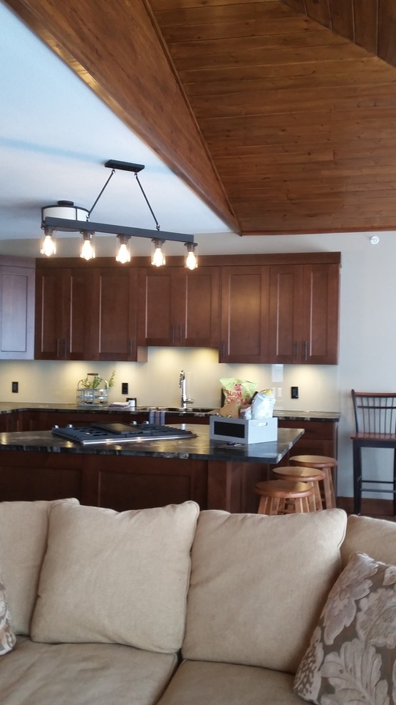 Example of a mid-sized mountain style l-shaped dark wood floor and brown floor eat-in kitchen design with an undermount sink, shaker cabinets, medium tone wood cabinets, granite countertops, beige backsplash, glass sheet backsplash, stainless steel appliances and an island