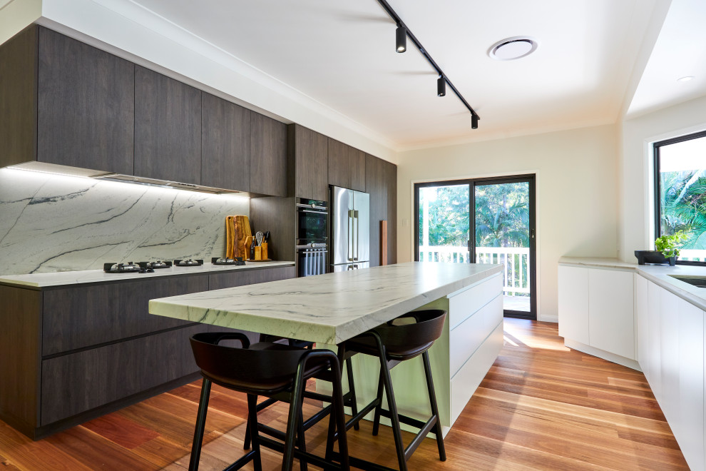 Photo of a large modern galley eat-in kitchen in Sunshine Coast with an integrated sink, raised-panel cabinets, dark wood cabinets, marble benchtops, white splashback, marble splashback, stainless steel appliances, light hardwood floors, with island, brown floor and white benchtop.