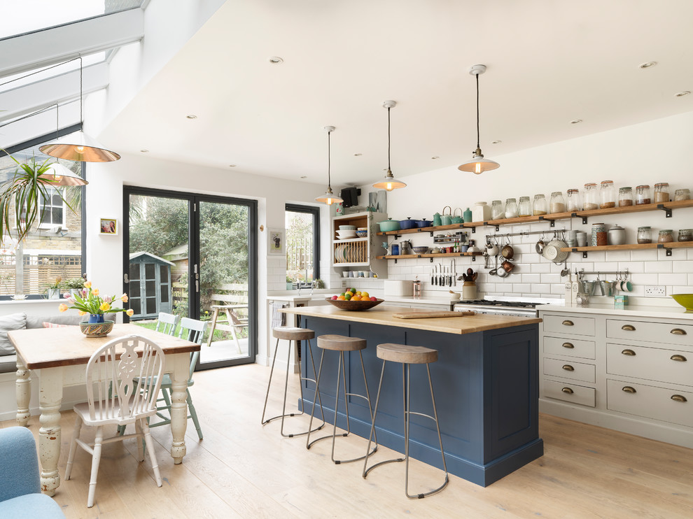 Inspiration for a transitional galley open plan kitchen in London with a farmhouse sink, flat-panel cabinets, grey cabinets, white splashback, subway tile splashback, stainless steel appliances, light hardwood floors, with island, beige floor and white benchtop.
