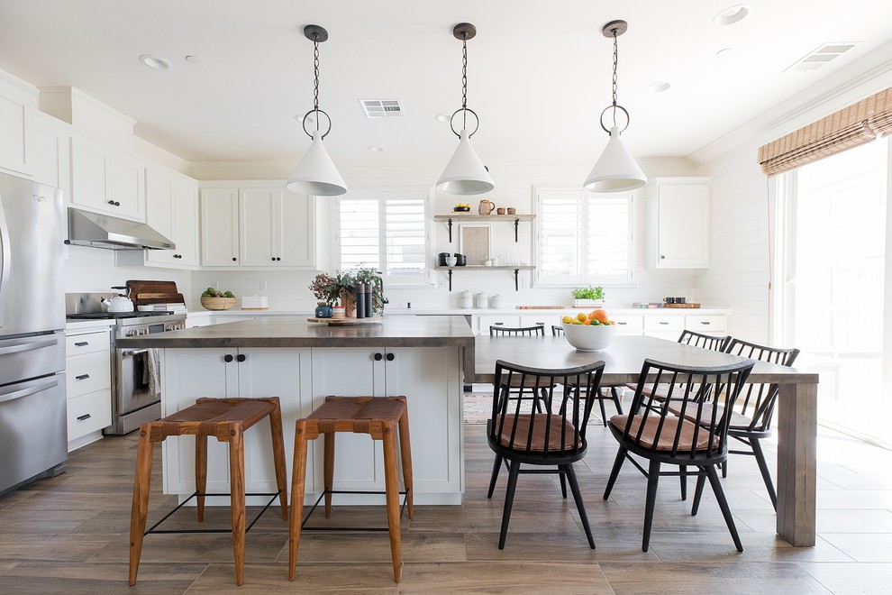 This is an example of a country l-shaped eat-in kitchen in Sacramento with shaker cabinets, white cabinets, wood benchtops, red splashback, subway tile splashback, stainless steel appliances, medium hardwood floors, with island, brown floor and brown benchtop.