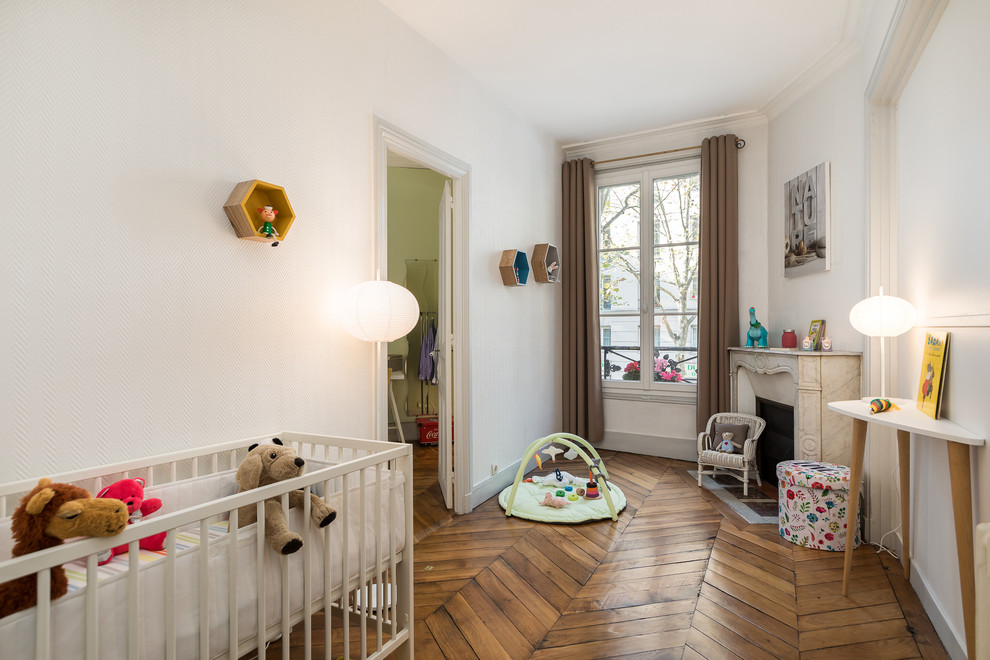 Cette image montre une chambre de bébé neutre design avec un mur blanc, un sol en bois brun et un sol marron.