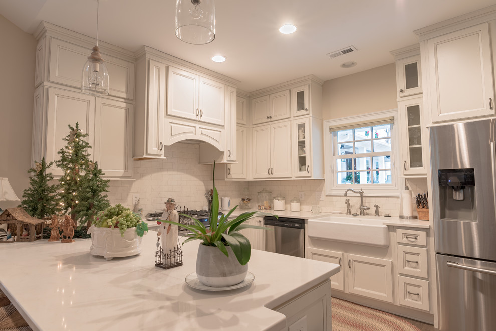 Example of a mid-sized transitional u-shaped medium tone wood floor eat-in kitchen design with a farmhouse sink, recessed-panel cabinets, white cabinets, solid surface countertops, white backsplash, stone tile backsplash, stainless steel appliances and a peninsula