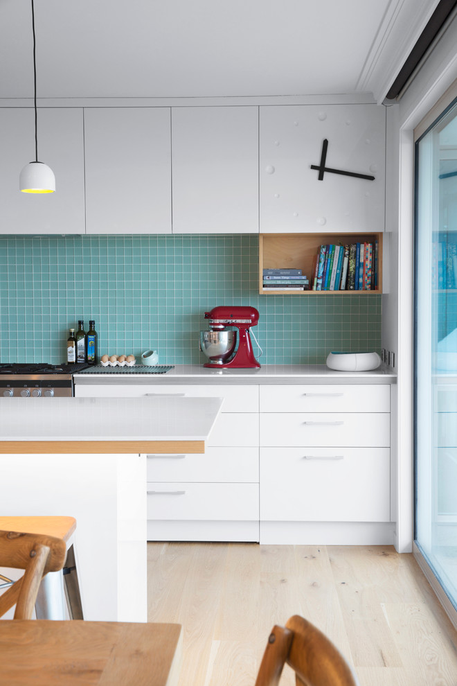 Inspiration for a mid-sized scandinavian u-shaped eat-in kitchen in Auckland with flat-panel cabinets, white cabinets, blue splashback, with island, mosaic tile splashback, light hardwood floors, a double-bowl sink and stainless steel appliances.