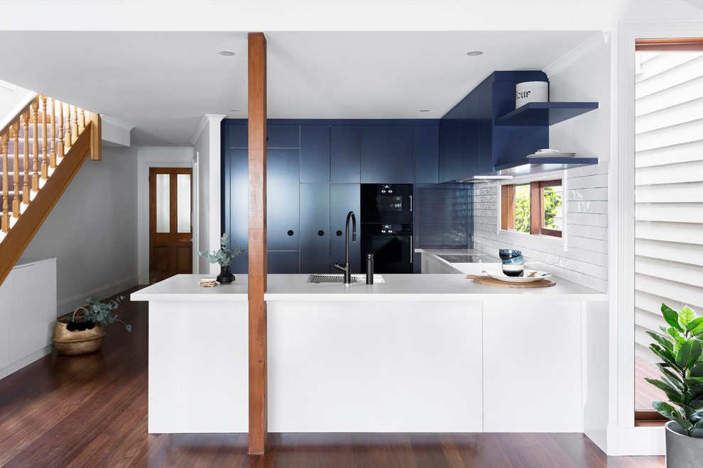 Inspiration for a mid-sized contemporary u-shaped eat-in kitchen in Melbourne with an undermount sink, flat-panel cabinets, blue cabinets, quartz benchtops, white splashback, window splashback, black appliances, dark hardwood floors, with island, brown floor and white benchtop.