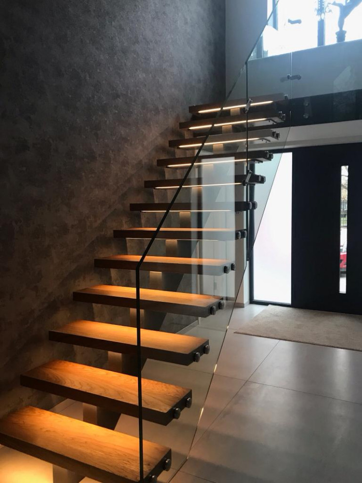 На фото: металлическая лестница на больцах, среднего размера в стиле модернизм с деревянными ступенями, стеклянными перилами и обоями на стенах