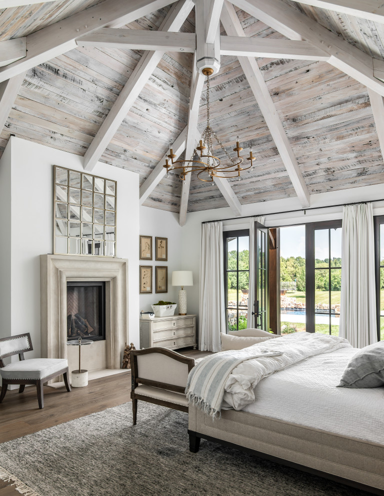 This is an example of a large transitional master bedroom in Nashville with white walls, medium hardwood floors, a standard fireplace and a stone fireplace surround.