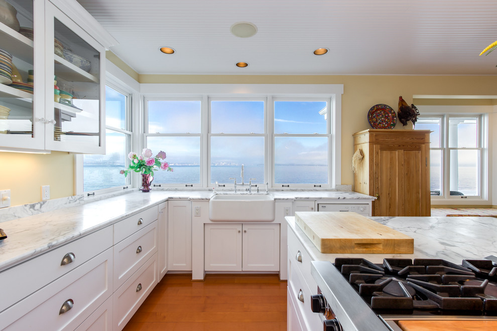 Design ideas for a large beach style u-shaped open plan kitchen in Seattle with a farmhouse sink, white cabinets, marble benchtops, stone slab splashback, white appliances, medium hardwood floors and with island.