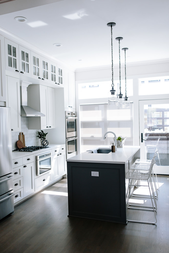Example of a mid-sized transitional galley dark wood floor and gray floor enclosed kitchen design in DC Metro with an undermount sink, recessed-panel cabinets, white cabinets, solid surface countertops, stainless steel appliances, an island, white countertops, white backsplash and subway tile backsplash