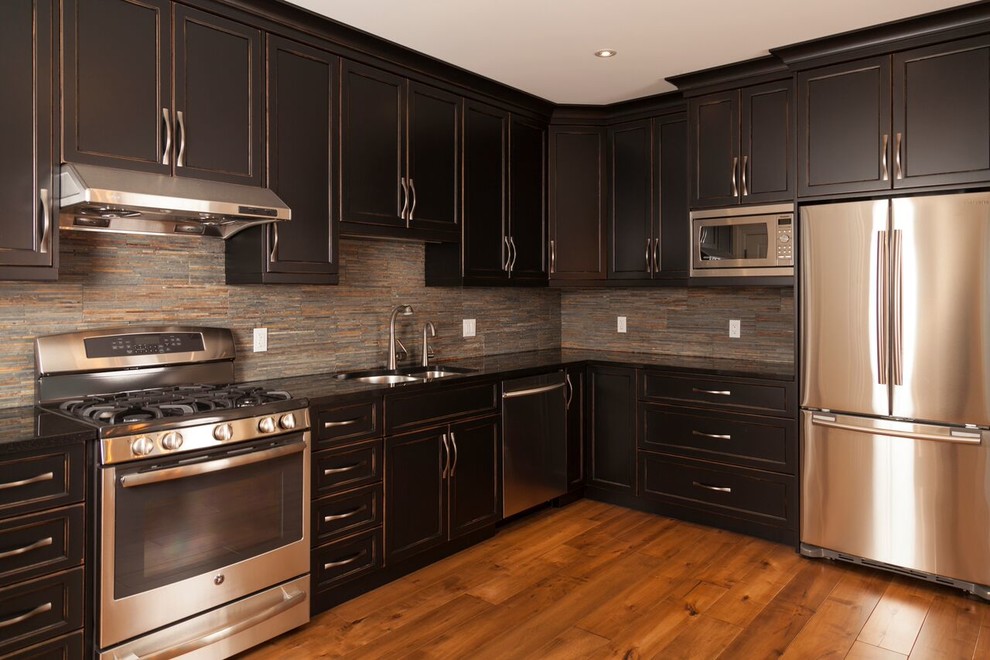 Mid-sized transitional l-shaped medium tone wood floor open concept kitchen photo in Toronto with a double-bowl sink, recessed-panel cabinets, dark wood cabinets, solid surface countertops, gray backsplash, stone tile backsplash, stainless steel appliances and no island