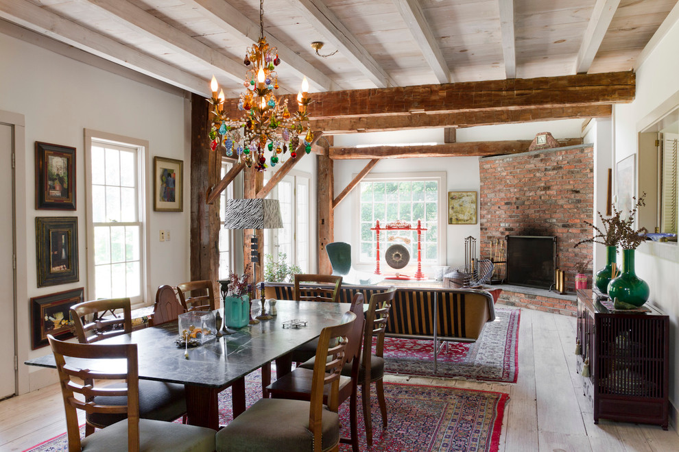 Eclectic open plan dining in New York with white walls, light hardwood floors, a corner fireplace and a brick fireplace surround.