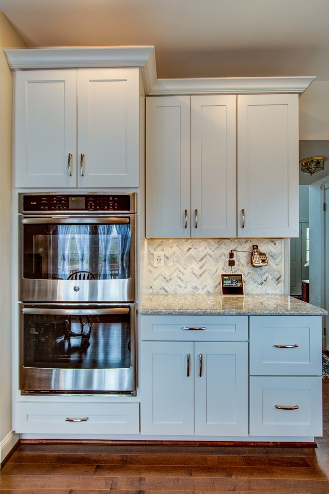 Example of a mid-sized transitional u-shaped dark wood floor and brown floor eat-in kitchen design in DC Metro with a farmhouse sink, shaker cabinets, white cabinets, stainless steel appliances, an island, gray countertops, quartzite countertops, white backsplash and mosaic tile backsplash