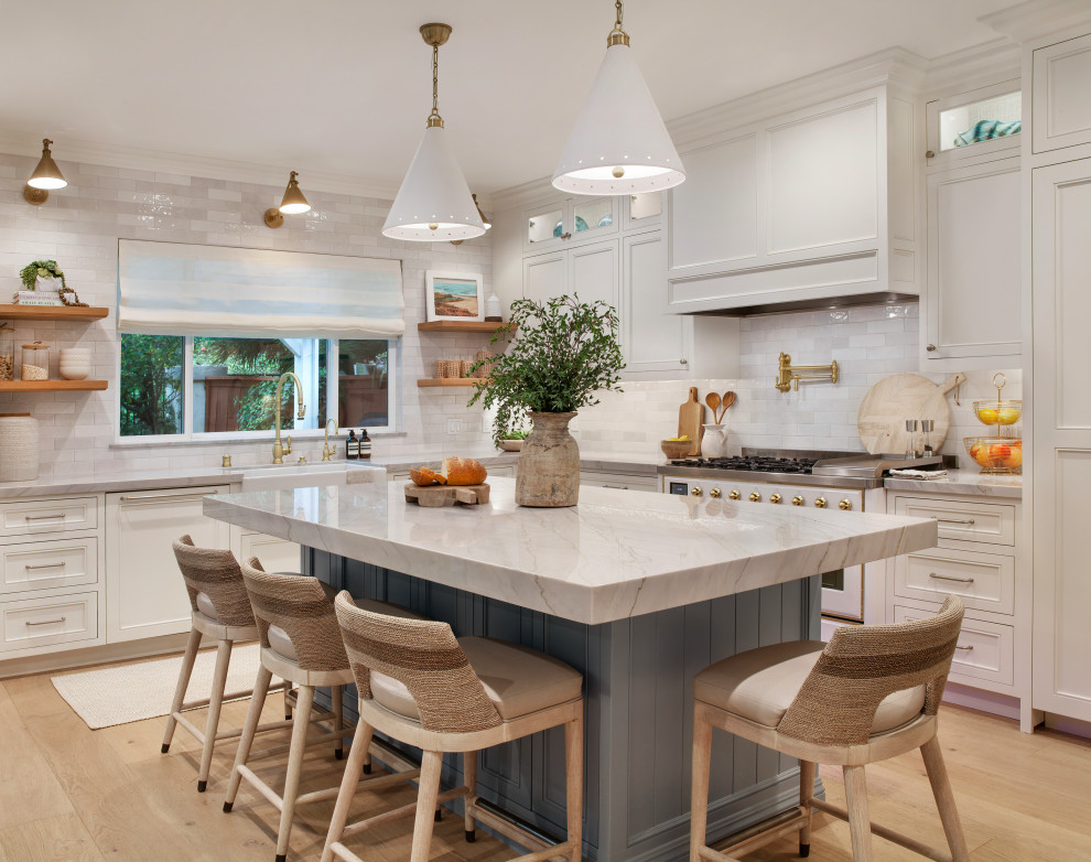 Inspiration for a large coastal l-shaped light wood floor open concept kitchen remodel in Orange County with a farmhouse sink, shaker cabinets, white cabinets, quartzite countertops, white backsplash, ceramic backsplash, paneled appliances and an island