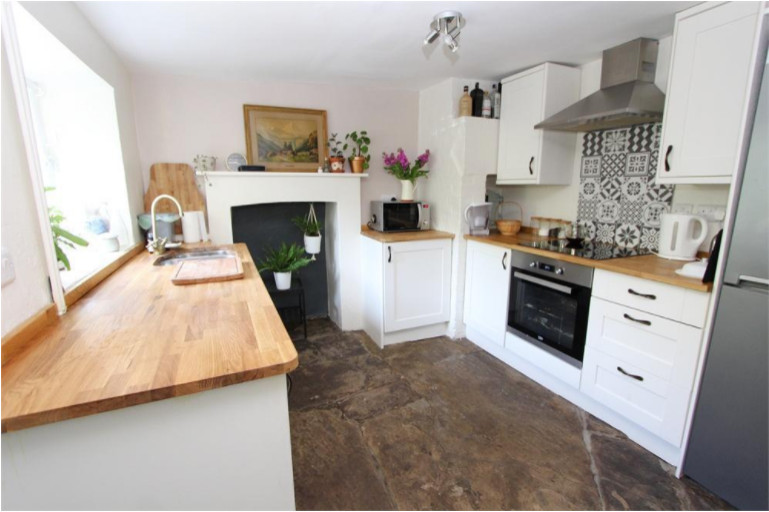 Photo of a small farmhouse galley enclosed kitchen in Other with a double-bowl sink, shaker cabinets, white cabinets, wood worktops, grey splashback, porcelain splashback, stainless steel appliances, limestone flooring, grey floors and a chimney breast.