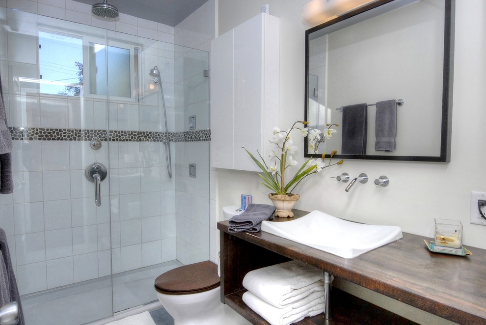 Photo of a modern master bathroom in Denver with open cabinets, medium wood cabinets, an alcove shower, a two-piece toilet, white tile, ceramic tile, white walls, a vessel sink and wood benchtops.