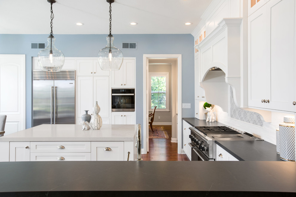 Inspiration for a large transitional u-shaped kitchen pantry in Tampa with a farmhouse sink, shaker cabinets, white cabinets, soapstone benchtops, white splashback, subway tile splashback, stainless steel appliances, dark hardwood floors, with island, brown floor and grey benchtop.