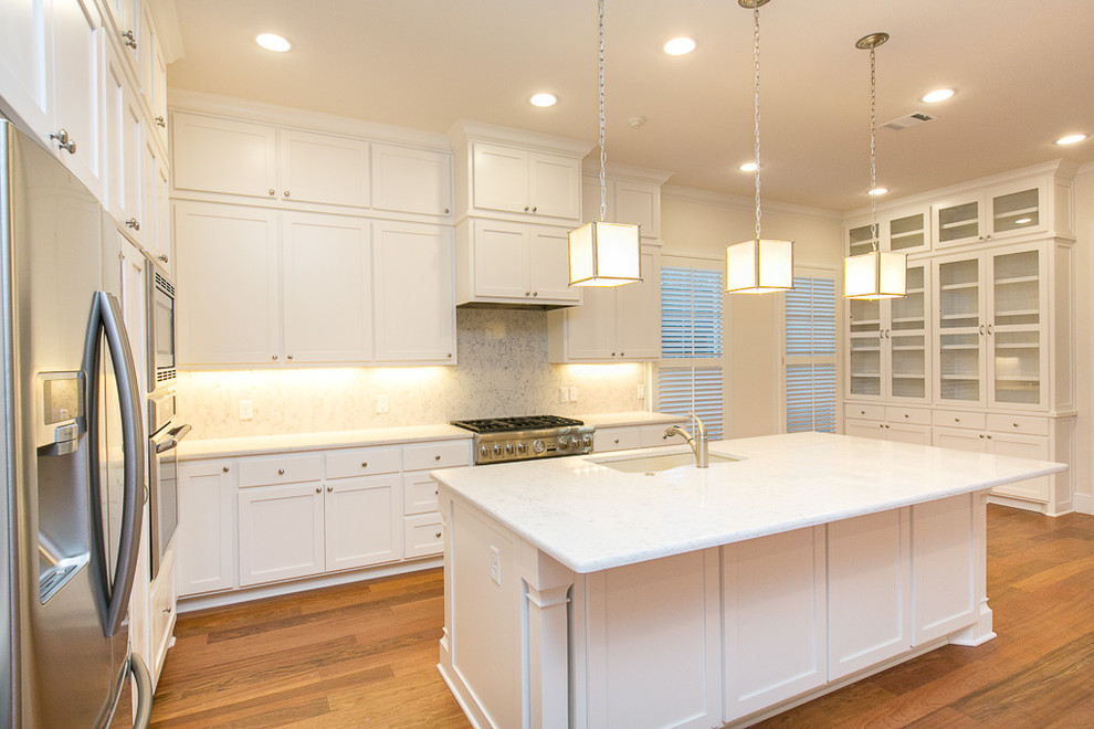 Photo of a traditional u-shaped open plan kitchen in Austin with an undermount sink, shaker cabinets, white cabinets, marble benchtops, grey splashback, porcelain splashback, stainless steel appliances, medium hardwood floors and with island.