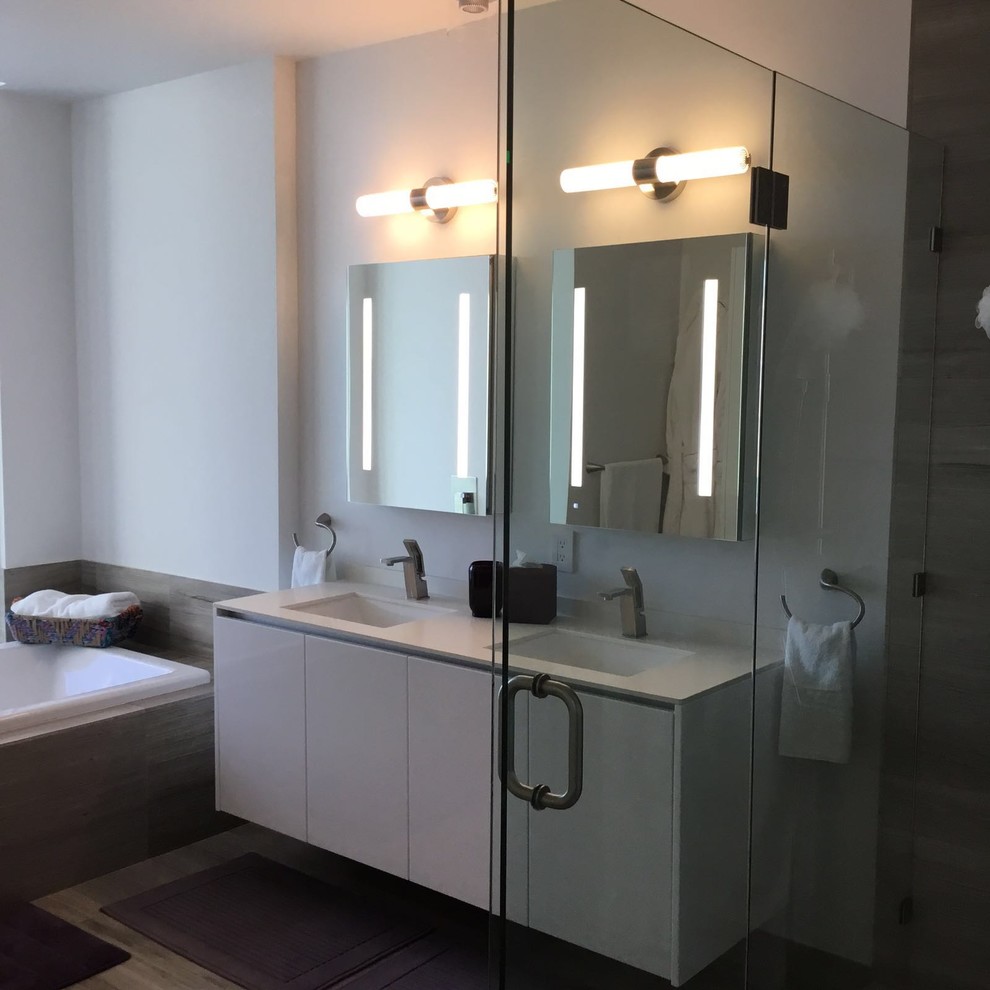 Inspiration for a mid-sized contemporary master bathroom in Miami with flat-panel cabinets, white cabinets, a drop-in tub, an alcove shower, white walls, ceramic floors, an undermount sink, solid surface benchtops, beige floor and a hinged shower door.